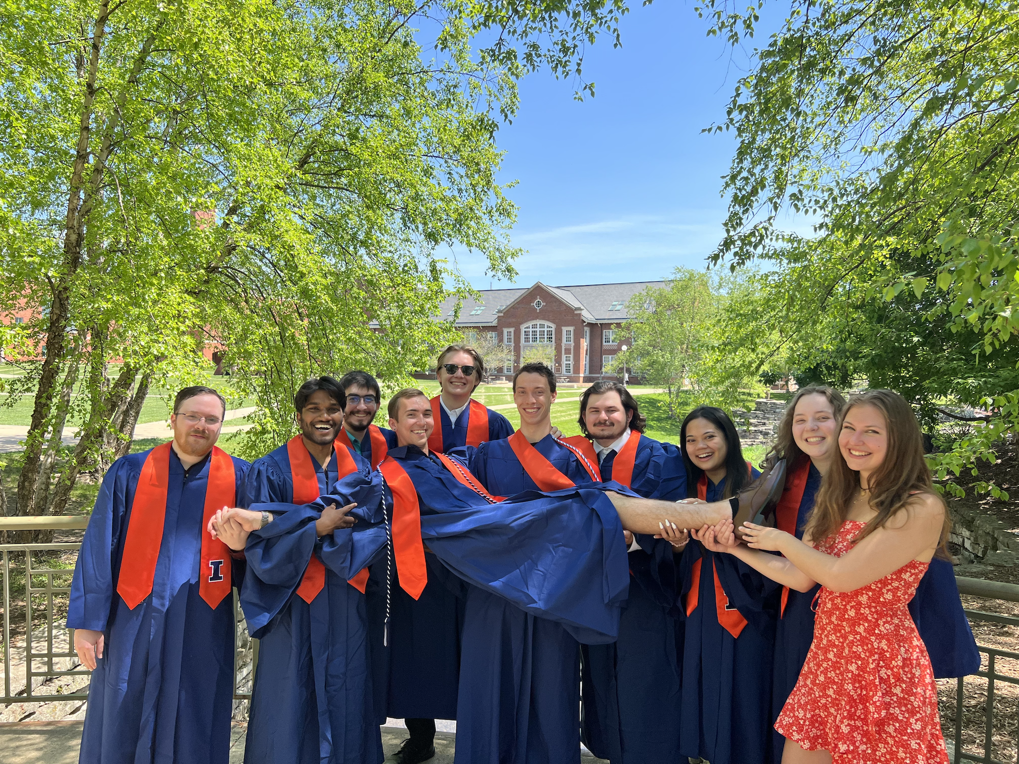 Group of students carrying Nathan Ryan in graduation robes.