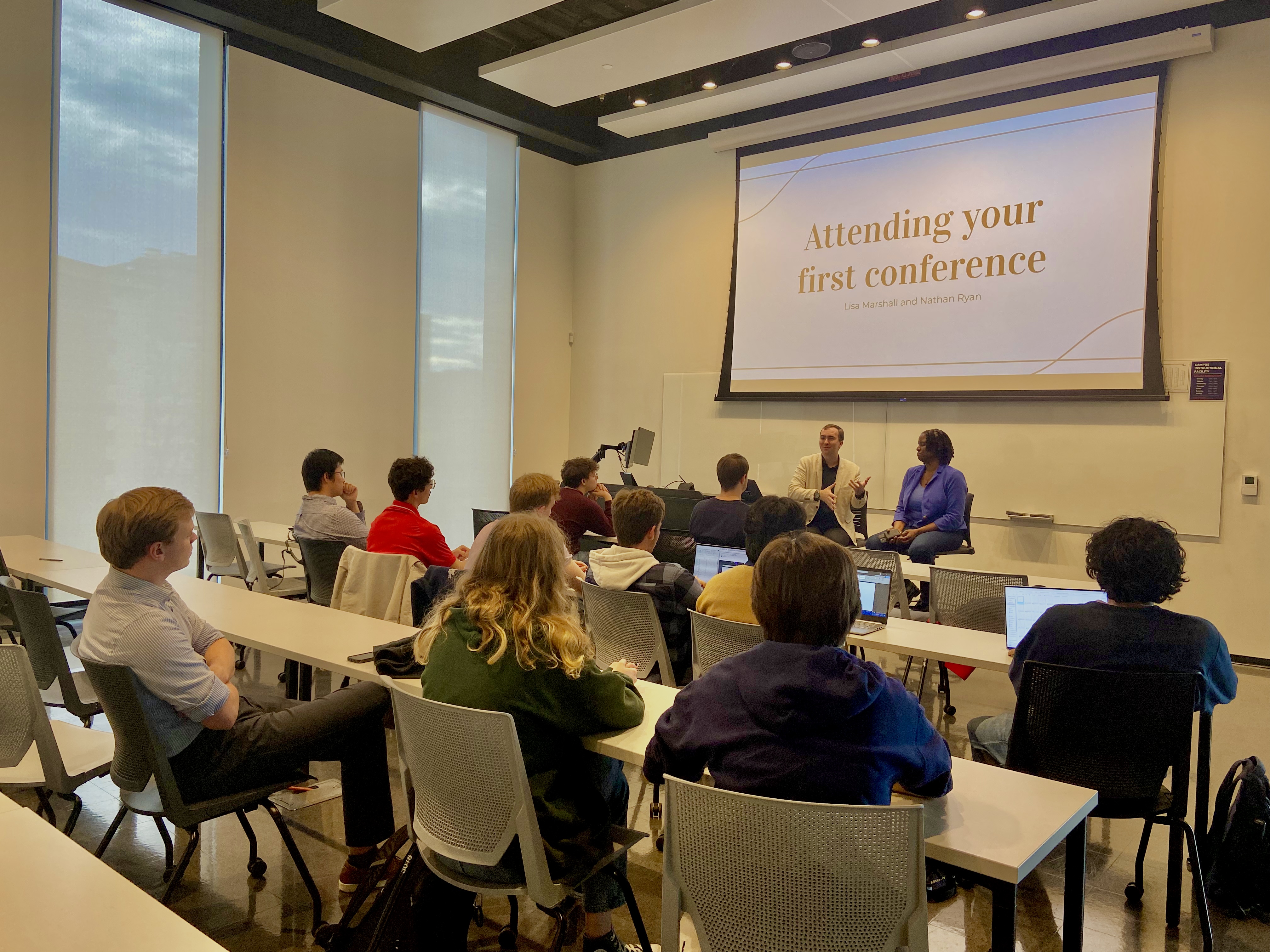 Nathan Ryan and Lisa Marshall sitting before a room full of students underneath a screen that reads 'Attending your first conference.'